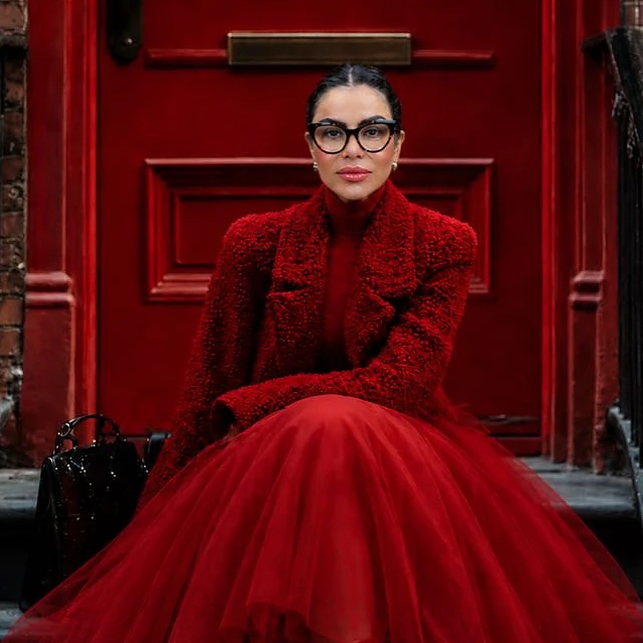 Dra. Luciana Vieira Coltri de vestido vermelho, sentada em frente a uma porta vermelha